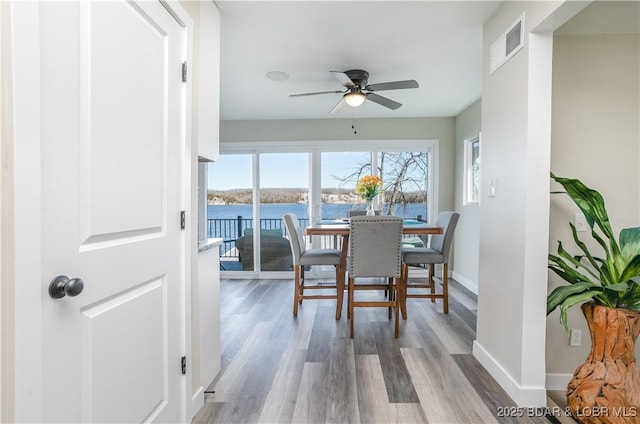 dining space featuring visible vents, a water view, ceiling fan, wood finished floors, and baseboards