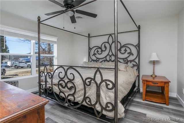 bedroom with a ceiling fan, visible vents, baseboards, and wood finished floors