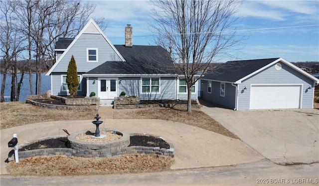 view of front facade with a garage, a water view, driveway, french doors, and a chimney