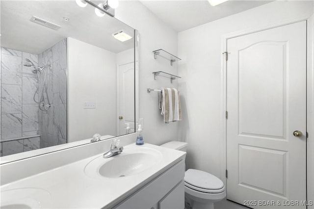 full bathroom featuring double vanity, visible vents, tiled shower, toilet, and a sink