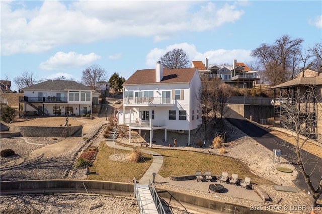 back of house featuring a chimney, dirt driveway, an outdoor fire pit, a balcony, and a residential view