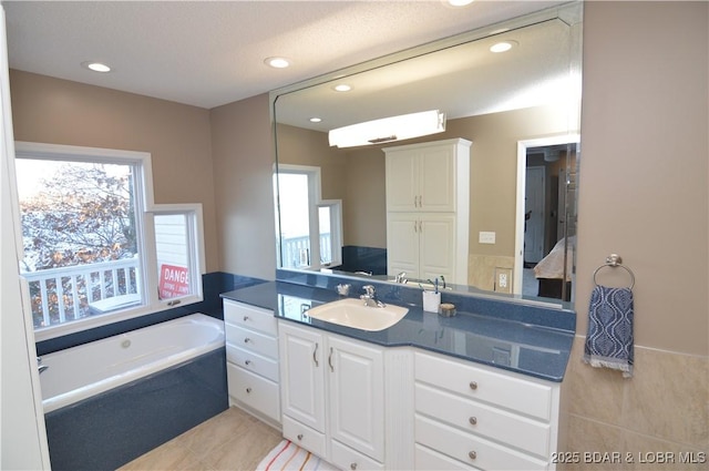 bathroom featuring a garden tub, vanity, and recessed lighting