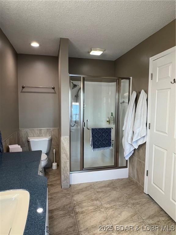 full bath with a textured ceiling, a stall shower, wainscoting, and tile walls