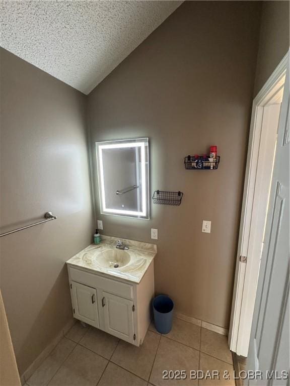 bathroom with lofted ceiling, vanity, a textured ceiling, tile patterned flooring, and baseboards