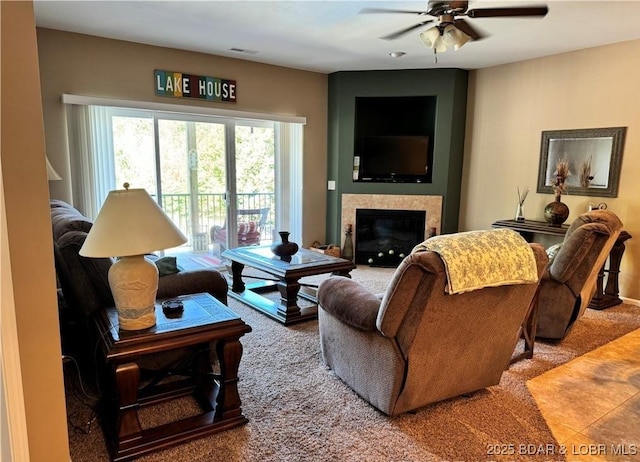 living room with tile patterned floors, visible vents, a ceiling fan, and a glass covered fireplace