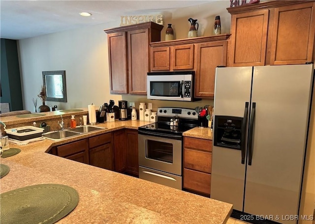 kitchen featuring stainless steel appliances, light countertops, brown cabinetry, a sink, and a peninsula