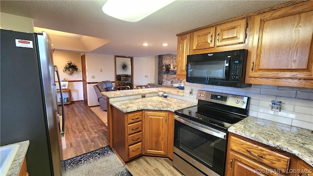 kitchen with light wood finished floors, a peninsula, appliances with stainless steel finishes, and backsplash