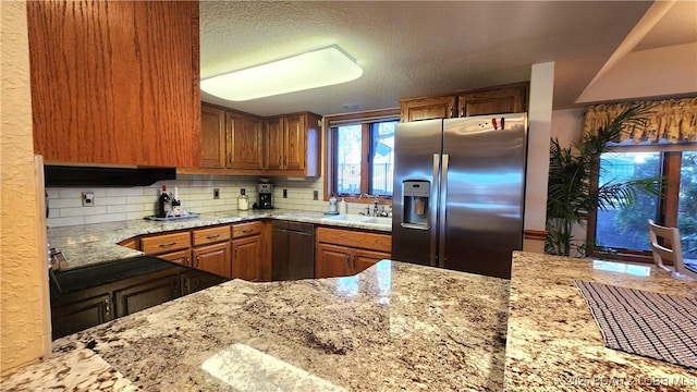 kitchen with light stone counters, black dishwasher, tasteful backsplash, a sink, and stainless steel fridge