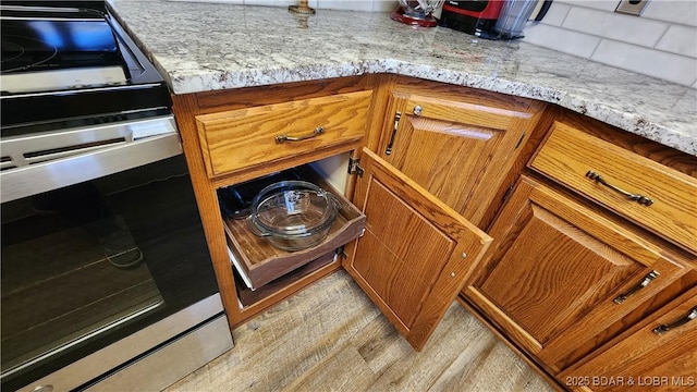 details with light wood-style floors, stainless steel electric range, light stone counters, and brown cabinets