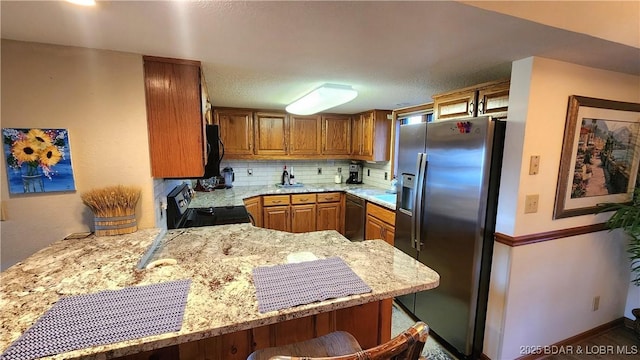 kitchen with black appliances, light stone counters, decorative backsplash, and brown cabinetry