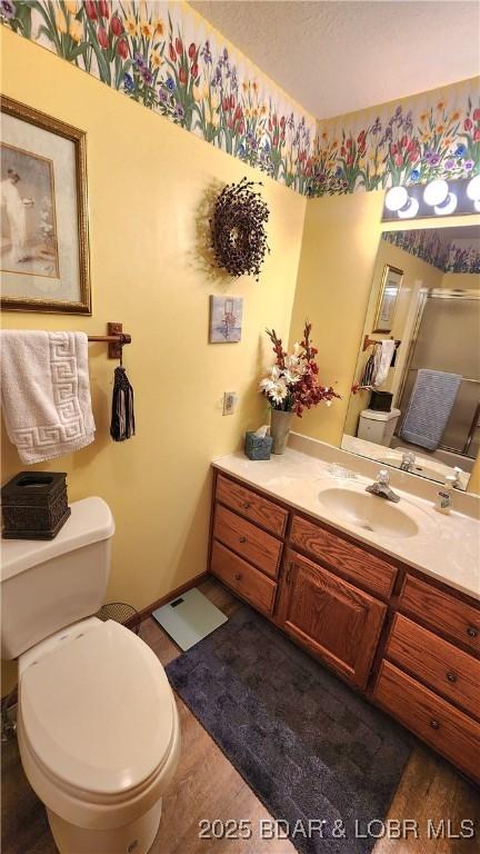 full bathroom featuring toilet, a shower with shower door, vanity, wood finished floors, and baseboards