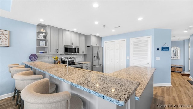 kitchen featuring open shelves, stainless steel appliances, gray cabinets, decorative backsplash, and light stone countertops