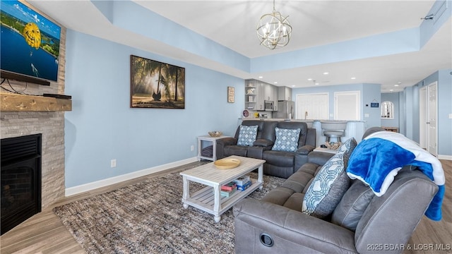 living area with a chandelier, a fireplace, wood finished floors, baseboards, and a tray ceiling