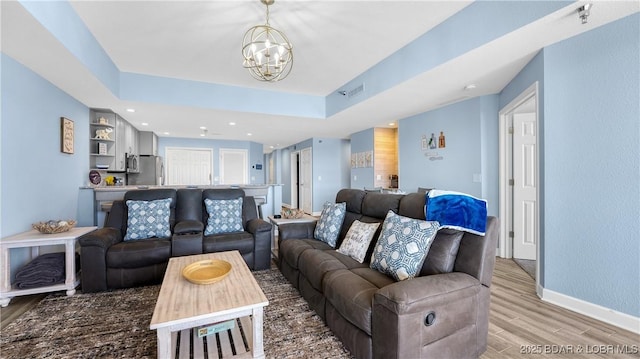 living area featuring a notable chandelier, light wood finished floors, a raised ceiling, visible vents, and baseboards