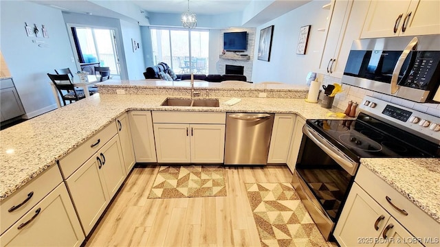 kitchen with light wood finished floors, stainless steel appliances, open floor plan, a sink, and a peninsula