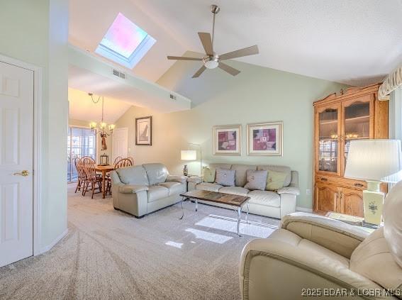 living room featuring light carpet, lofted ceiling with skylight, visible vents, and ceiling fan with notable chandelier