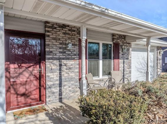 doorway to property featuring a porch and brick siding