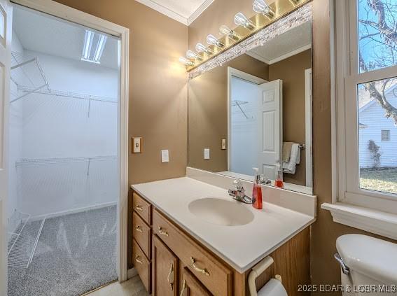 half bathroom featuring ornamental molding, a healthy amount of sunlight, vanity, and toilet