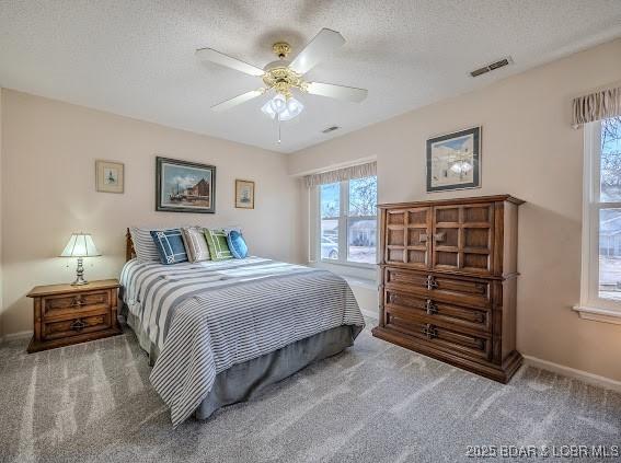 bedroom featuring carpet floors, visible vents, ceiling fan, a textured ceiling, and baseboards