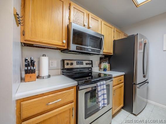 kitchen featuring stainless steel appliances, light countertops, baseboards, and light tile patterned floors