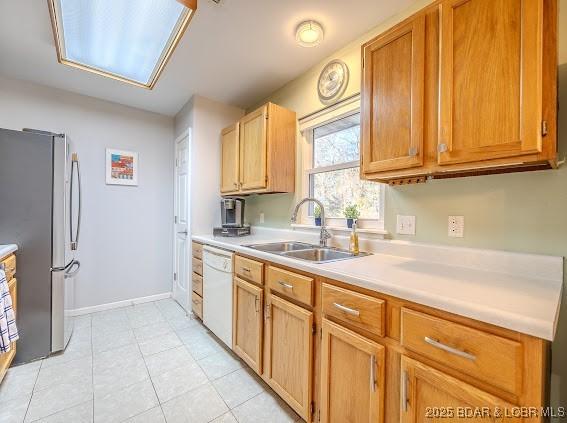 kitchen featuring baseboards, dishwasher, freestanding refrigerator, light countertops, and a sink