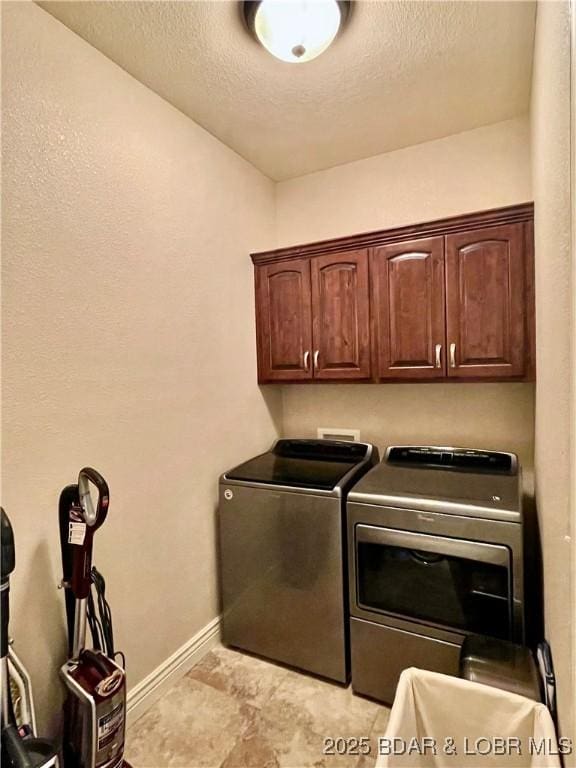 washroom featuring cabinet space, washing machine and dryer, baseboards, and a textured ceiling