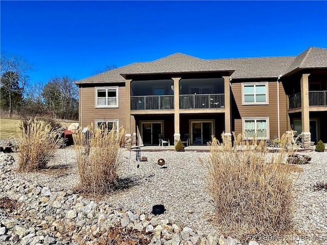 rear view of property featuring a shingled roof, a patio area, and a balcony