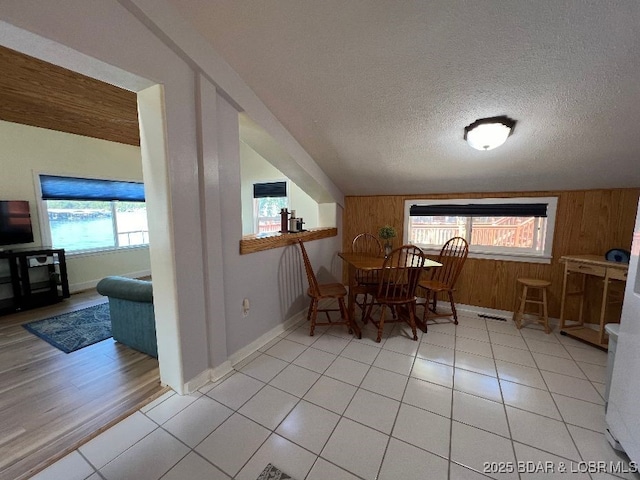 dining area with light tile patterned flooring, plenty of natural light, wooden walls, and a textured ceiling