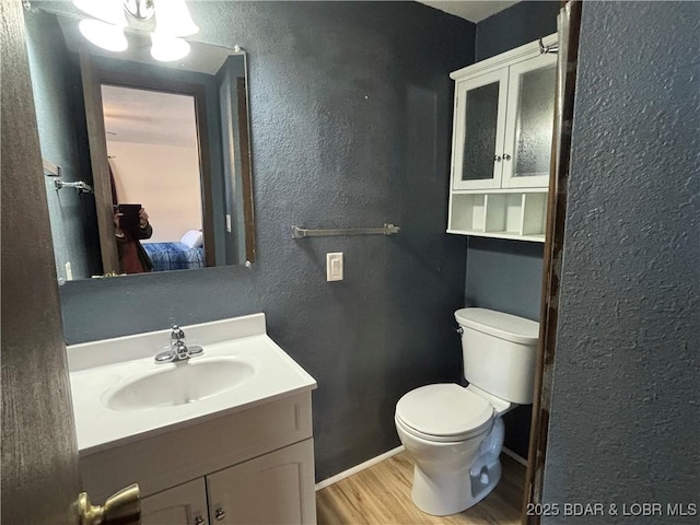 bathroom with toilet, vanity, wood finished floors, and a textured wall