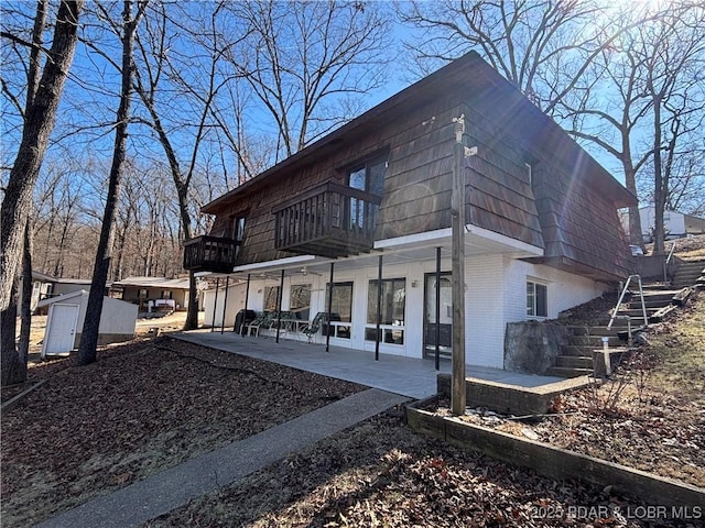 view of home's exterior featuring a patio area, brick siding, a balcony, and mansard roof