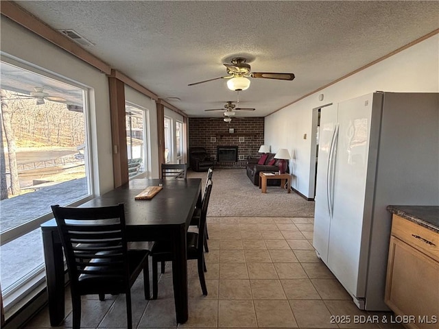 dining room featuring visible vents, ceiling fan, a textured ceiling, a brick fireplace, and light tile patterned flooring