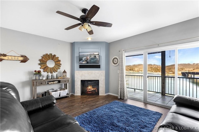 living room featuring a ceiling fan, a fireplace, baseboards, and wood finished floors