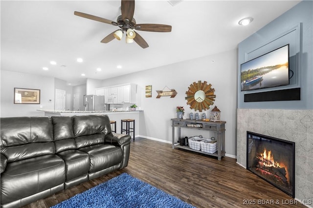 living area featuring baseboards, a ceiling fan, a tile fireplace, wood finished floors, and recessed lighting