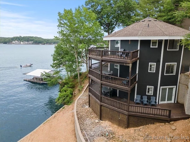 back of property with a shingled roof and a deck with water view