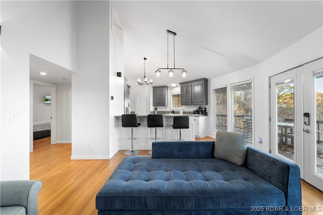 living area with light wood finished floors, a notable chandelier, baseboards, and high vaulted ceiling