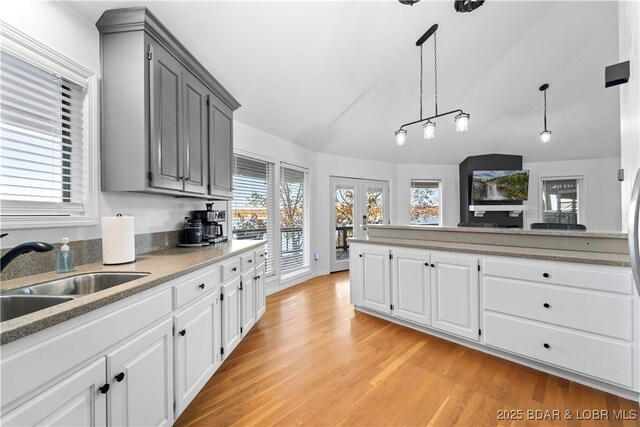 kitchen featuring a sink, vaulted ceiling, hanging light fixtures, gray cabinets, and light wood finished floors