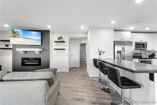 living area with recessed lighting, a glass covered fireplace, light wood-style flooring, and baseboards