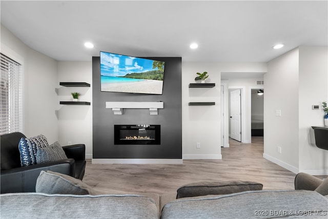 living area featuring a glass covered fireplace, recessed lighting, baseboards, and wood finished floors