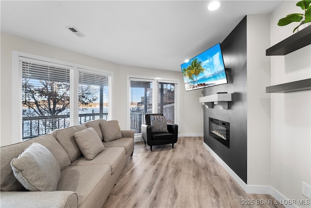 living room featuring light wood-style flooring, visible vents, baseboards, and a glass covered fireplace