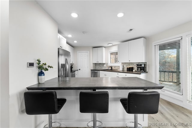 kitchen with dark countertops, appliances with stainless steel finishes, a sink, a peninsula, and a kitchen bar