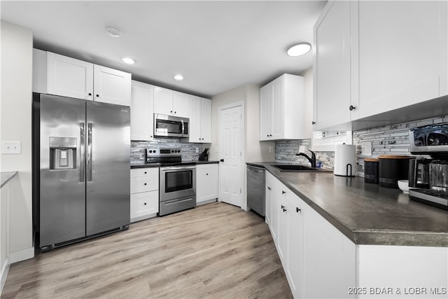 kitchen featuring stainless steel appliances, dark countertops, a sink, and white cabinetry