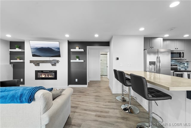 living area with baseboards, recessed lighting, a glass covered fireplace, and light wood-style floors