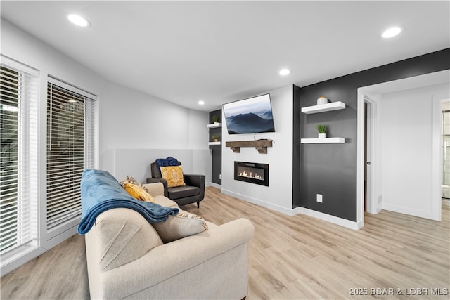 living room featuring a large fireplace, light wood-style flooring, baseboards, and recessed lighting