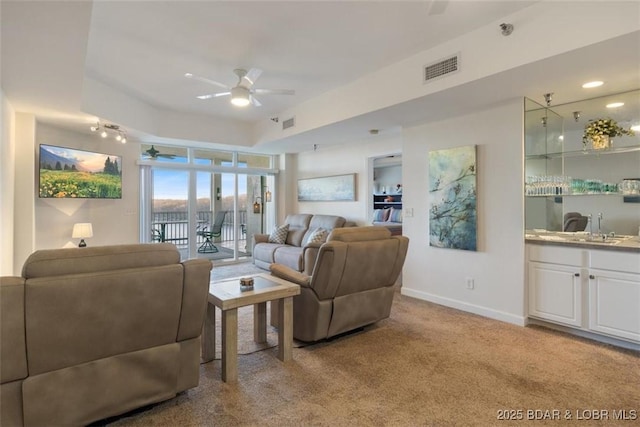 living area featuring ceiling fan, light carpet, baseboards, and bar area