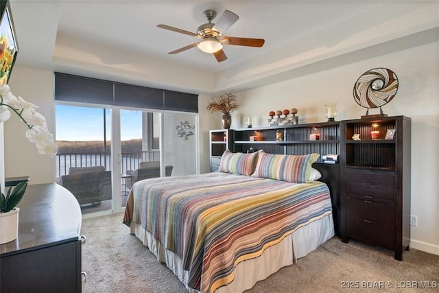 carpeted bedroom with access to outside, a tray ceiling, baseboards, and a ceiling fan