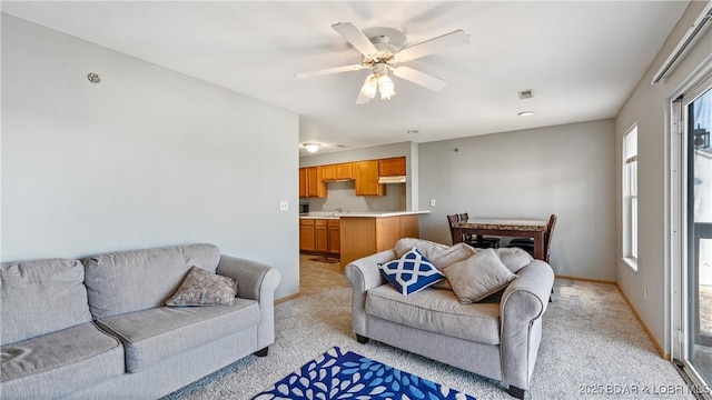 living room with ceiling fan, visible vents, baseboards, and light colored carpet