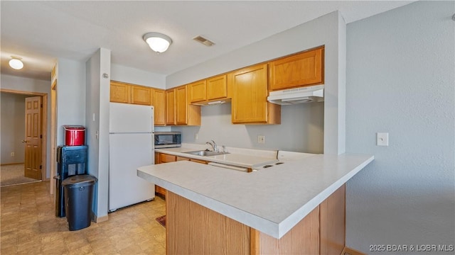 kitchen featuring light countertops, stainless steel microwave, freestanding refrigerator, a sink, and under cabinet range hood