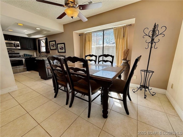 dining room with light tile patterned floors, baseboards, ceiling fan, a tray ceiling, and a textured ceiling