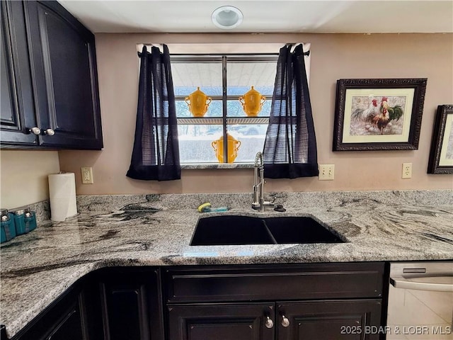 kitchen with dishwasher, dark cabinets, light stone counters, and a sink