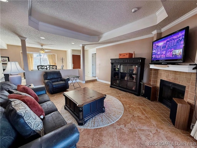 tiled living room featuring crown molding, a tile fireplace, a raised ceiling, and ornate columns